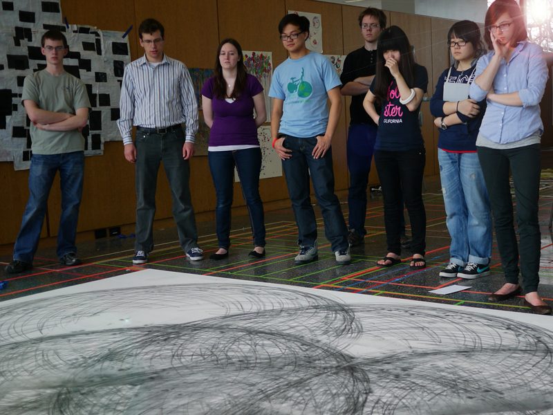Students gathered around a large floor drawing during a creativity exercise.