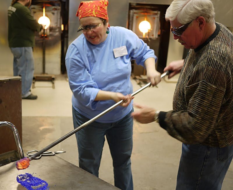 Grandpa is rolling his molten glass into bits of colored glass. Next he is going to mush it onto the vase...with the help of two master glass blowers.