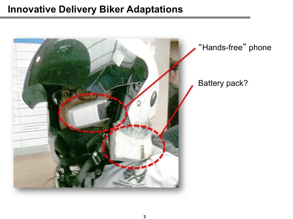 Field observation of a delivery biker's helmet with a 'hands-free' handset mounted to the visor and a battery pack taped below, illustrating improvised tech adaptations observed in the field.