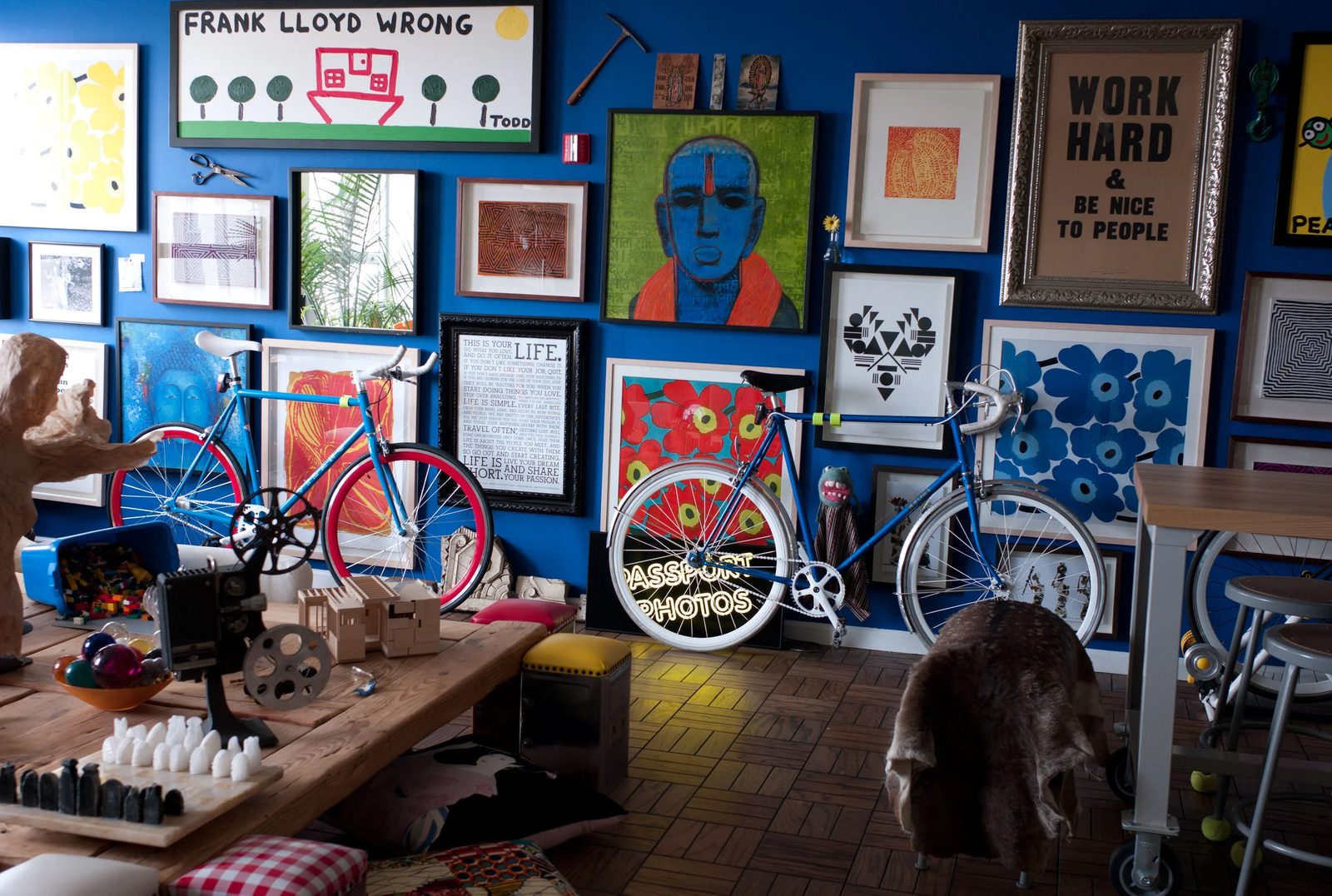 Eclectic creative studio interior with a blue gallery wall of framed artworks and two bicycles, conveying a design-thinking mindset of curiosity and visual inspiration.